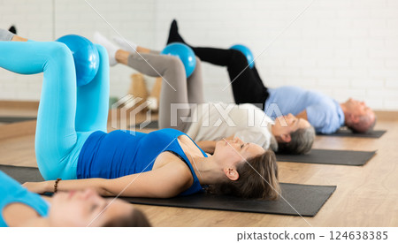 Middle-aged woman practicing pilates with ball in gym area 124638385