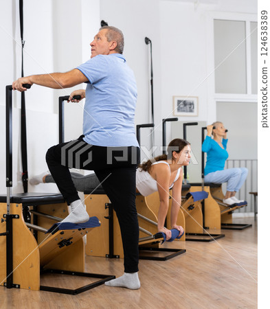 Mature man performing standing Pilates exercise on Wanda chair in fitness studio 124638389