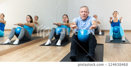 Senior man doing sit-ups with pilates ball at gym Senior man doing sit-ups with pilates ball at gym 124638468