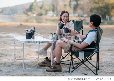 Friends enjoying coffee while camping by a serene lakeside, surrounded by nature and tranquility. 124640023