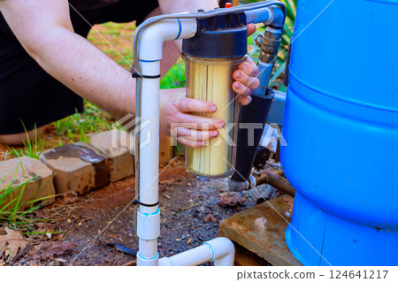 Individual works on connecting water filter to garden water system in residential outdoor setting. 124641217