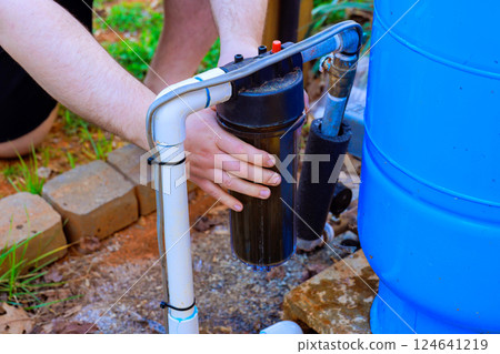 Person changing water filter connected to rainwater collection system outdoors in garden setting. 124641219