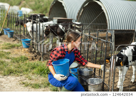 Portrait of farmer girl with bucket against the background of calf pen on summer day 124642034