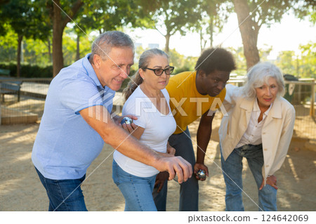 A group of multiracial mature adult people playing patanque game outdoors in a park 124642069