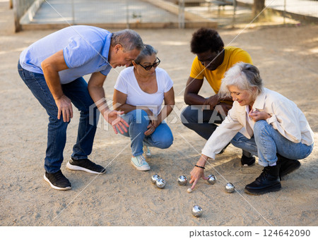 Positive mature diverse percioners comparing the distance of pumped balls after petangue at the sunny afternoon outdoors Positive mature diverse percioners comparing the distance of pumped balls after petangue at the sunny afternoon outdoors 124642090