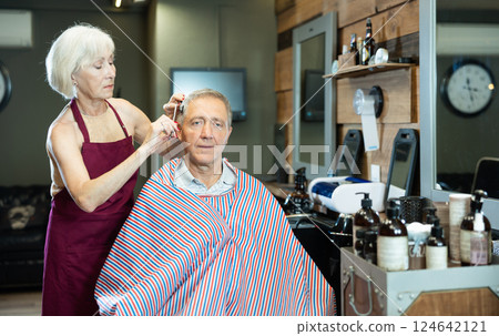 Experienced female hairdresser cutting hair of elderly client with scissors in barbershop Experienced female hairdresser cutting hair of elderly client with scissors in barbershop 124642121