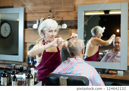 Haircut in a stylish barbershop - an elderly man sits in a chair, woman cuts her hair and does hair styling 124642132