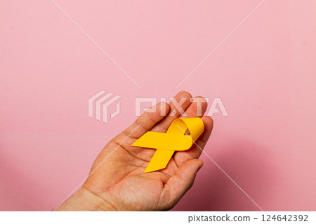Raising awareness for cancer with a yellow ribbon on a pink background 124642392