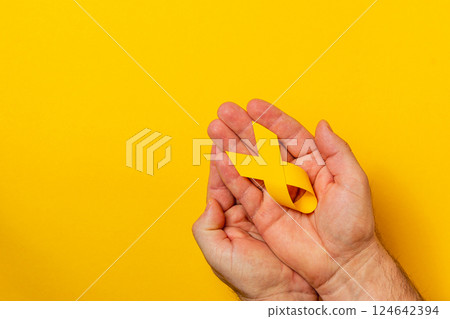 Hands holding a yellow ribbon symbolizing cancer awareness and support Hands holding a yellow ribbon symbolizing cancer awareness and support 124642394
