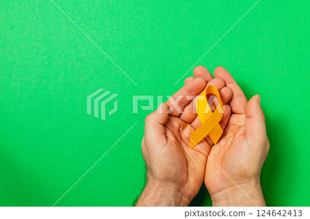 Hands holding a yellow ribbon symbolizing awareness and support for cancer Hands holding a yellow ribbon symbolizing awareness and support for cancer 124642413