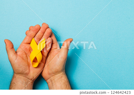Holding a yellow ribbon of hope in the fight against cancer awareness Holding a yellow ribbon of hope in the fight against cancer awareness 124642423