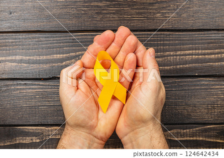 Hands holding a yellow ribbon symbolizing cancer awareness and hope Hands holding a yellow ribbon symbolizing cancer awareness and hope 124642434