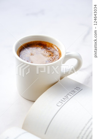 The image of someone reading a paperback while drinking coffee. The image of someone reading a paperback while drinking coffee. 124643034