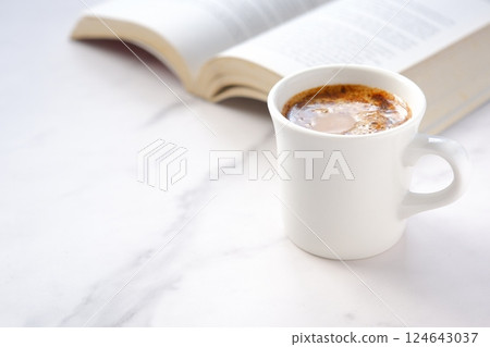 一個人一邊喝咖啡一邊悠閒地閱讀平裝書的圖像。 一個人一邊喝咖啡一邊悠閒地閱讀平裝書的圖像。 124643037