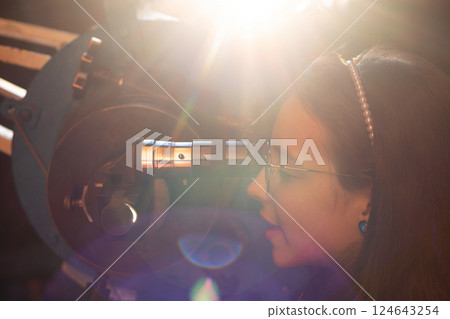 Girl looks through telescope with bright sunlight flare. Girl looks through telescope with bright sunlight flare. 124643254