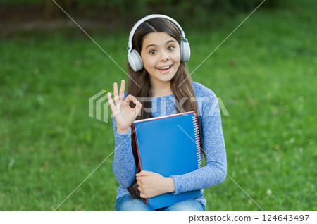 School education. Teen girl in audio headphones. Student listen audiobook. Homework education. Ok gesture. Back to school. Student girl listen audiobook. School education for girl. Student lifestyle 124643497