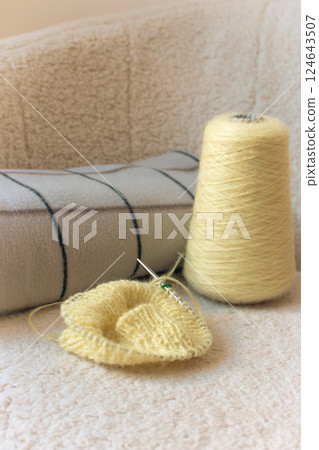 Yellow knitting with grey checkered plaid on sofa. Knitted fashion. Cotton knitting crochet with knitting needles and bobbin. Knitting hobby. Handmade knitted clothing. Cozy still life. Domestic life 124643507