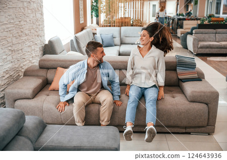 Sitting and testing product. Couple choosing the sofa and bed in the store 124643936
