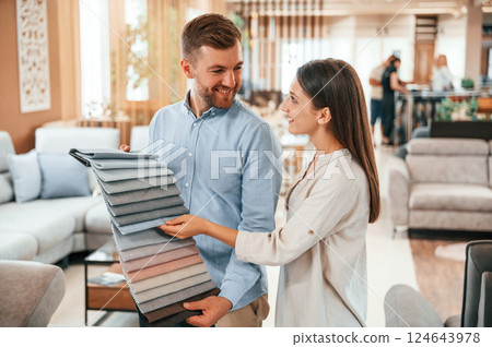 Man holding different colored materials to choose from. Couple looking for the sofa and bed in the store 124643978