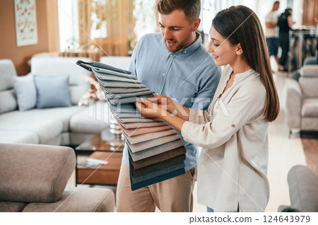 Man holding different colored materials to choose from. Couple looking for the sofa and bed in the store 124643979