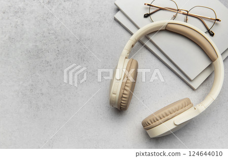 Modern wireless headphones lying on table next to books and eyeglasses Modern wireless headphones lying on table next to books and eyeglasses 124644010
