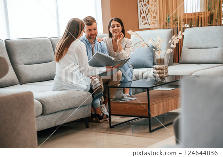 Sitting together. Woman helping couple with choosing the sofa and bed in the store 124644036