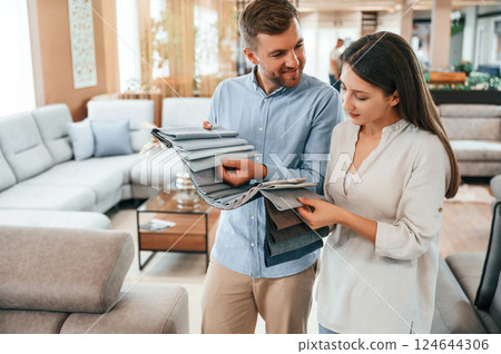 Man holding different colored materials to choose from. Couple looking for the sofa and bed in the store 124644306