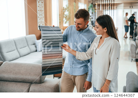 Man holding different colored materials to choose from. Couple looking for the sofa and bed in the store Man holding different colored materials to choose from. Couple looking for the sofa and bed in the store 124644307