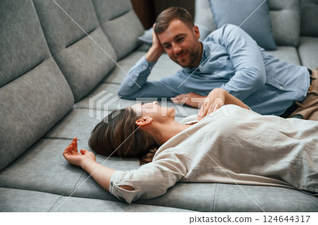 Side view. Laying down together. Couple choosing the sofa and bed in the store Side view. Laying down together. Couple choosing the sofa and bed in the store 124644317