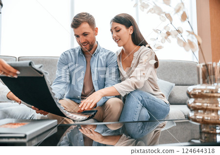 Looking at the catalogue. Woman helping couple with choosing the sofa and bed in the store Looking at the catalogue. Woman helping couple with choosing the sofa and bed in the store 124644318