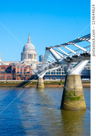 Visitors stroll across Millennium Bridge with stunning views of St. Paul's Cathedral. The clear blue sky enhances the architectural beauty of both the bridge and the iconic dome. 124644624