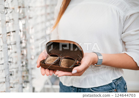 In brown colored case. Woman holding glasses in hands in the store. Close up view 124644703