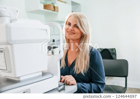 Woman is sitting in the clinic and checking her vision by special device 124644897