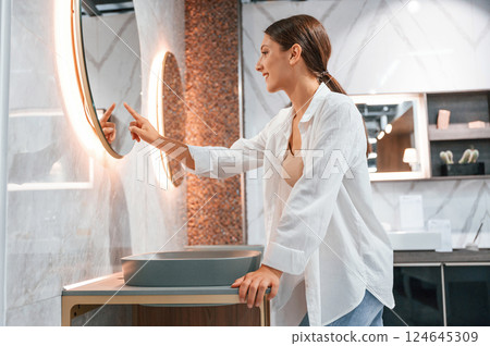 Using the mirror with touchscreen feature. Pretty young woman is in the store of goods for the home 124645309