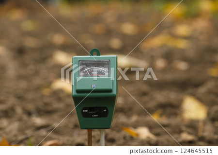 Close-up of a green soil moisture meter in a garden setting with blurred muddy background, Close-up of a green soil moisture meter in a garden setting with blurred muddy background, 124645515