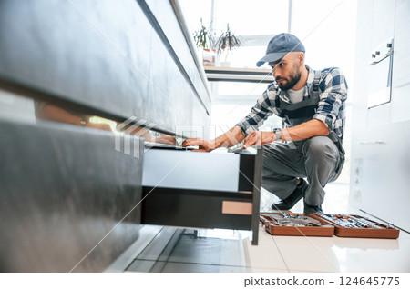 Case with equipment. Plumber in uniform is indoors at home 124645775