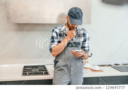 Holding smartphone in hand. Plumber in uniform is indoors at home 124645777