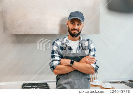 Standing with arms crossed. Plumber in uniform is indoors at home 124645778