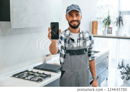 Holding smartphone in hand. Plumber in uniform is indoors at home 124645780