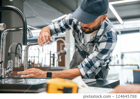 Works with sink. Plumber in uniform is indoors at home Works with sink. Plumber in uniform is indoors at home 124645788