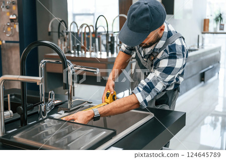 Works with sink. Plumber in uniform is indoors at home 124645789