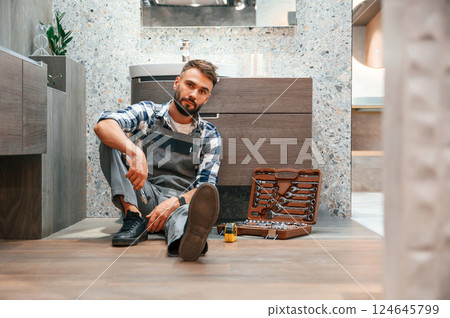 On the floor with case of equipment. Plumber in uniform is indoors at home 124645799