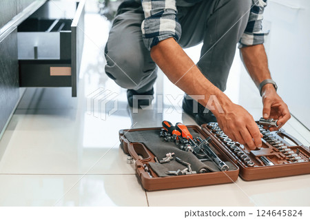 Close up view. Taking tools. Plumber in uniform is indoors at home 124645824