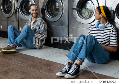Man and woman communicating and completing their routine washing chore in public laundromat service Man and woman communicating and completing their routine washing chore in public laundromat service 124648098