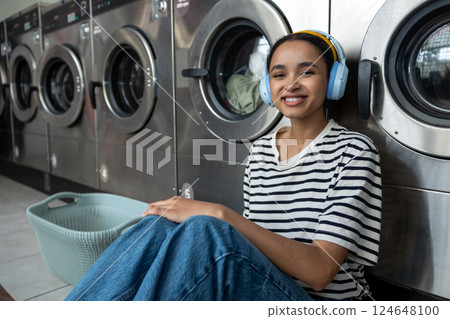 Woman sitting in public laundromat wearing headphones while waiting for washing machine Woman sitting in public laundromat wearing headphones while waiting for washing machine 124648100