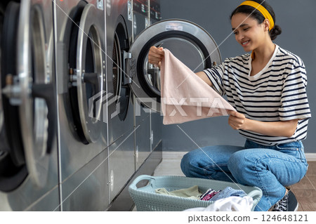 Woman in laundromat folding freshly washed clothes after using coin-operated appliance Woman in laundromat folding freshly washed clothes after using coin-operated appliance 124648121