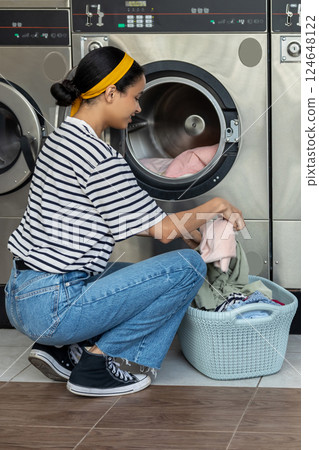 Woman placing dirty clothes into commercial washing machine Woman placing dirty clothes into commercial washing machine 124648122