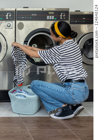 Female customer in laundry shop using washer for washing dirty household laundry 124648124