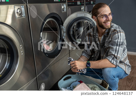 Positive man in self service commercial laundry using washing and drying machine 124648137