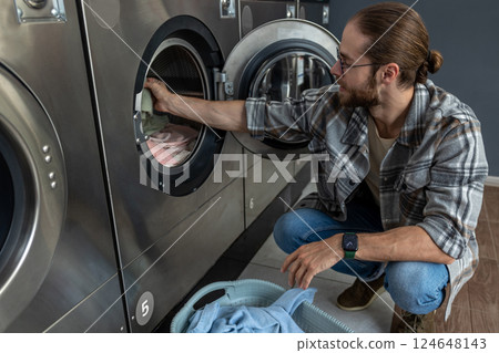 Positive man in self service commercial laundry using washing and drying machine 124648143